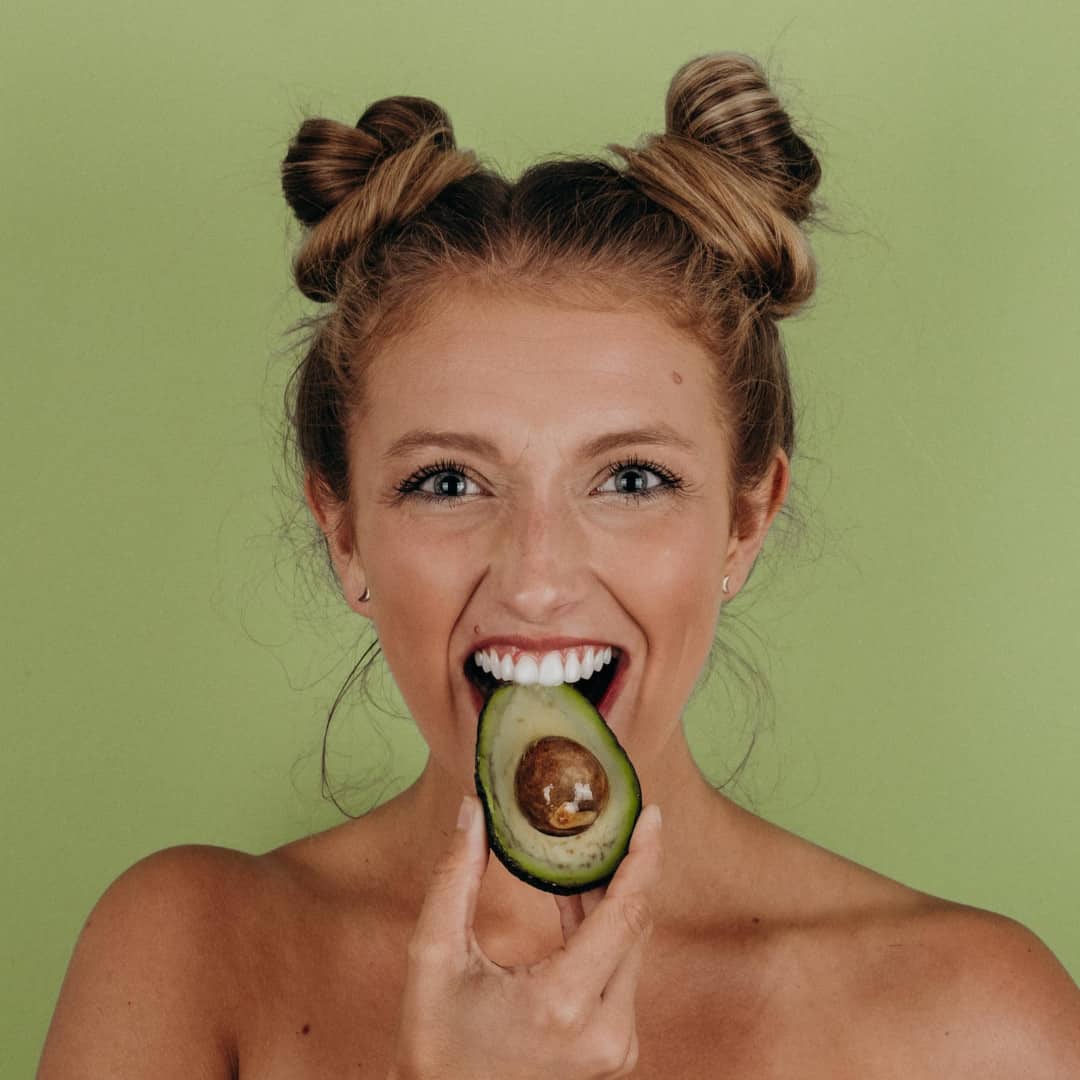 Happy woman biting into an avocado - Keto Diet vs Metabolic Balance