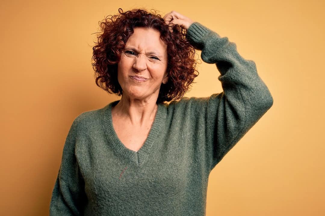 A mature woman with short red hair, scatching her head as she's frustrated about losing weight after 45